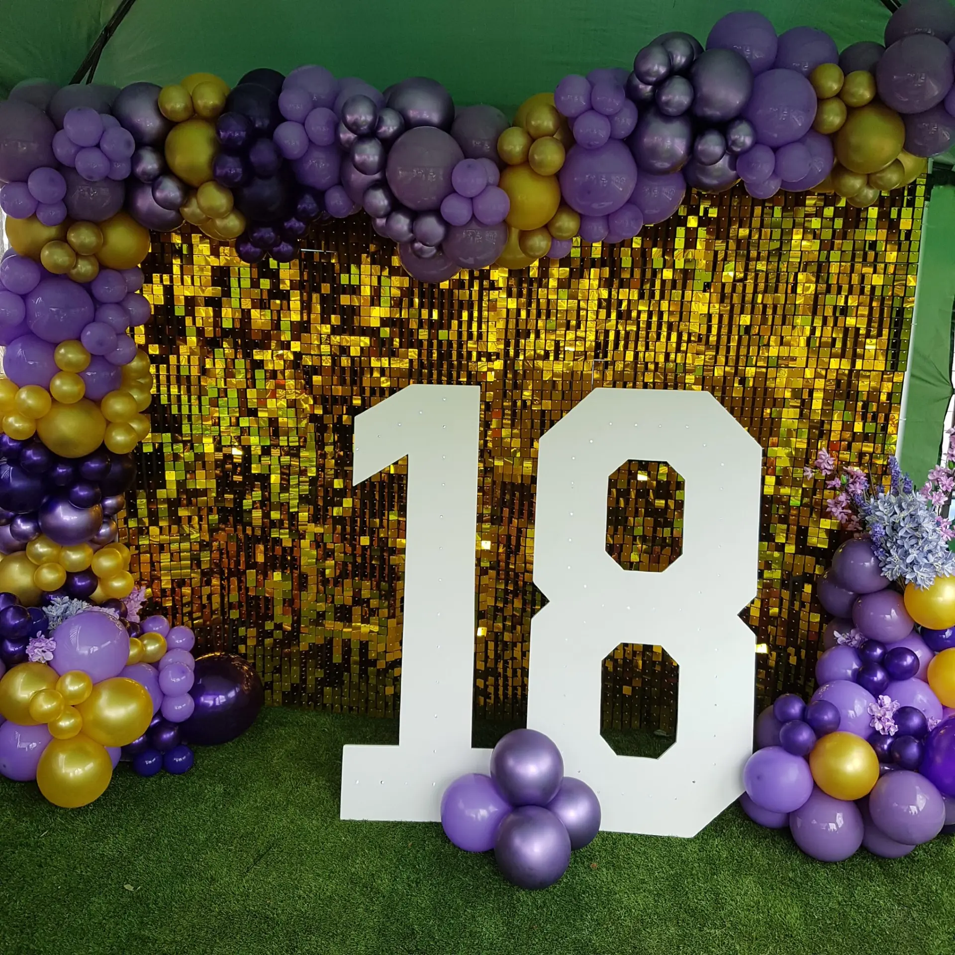 Purple and gold balloon garland framing a gold backdrop and large number eighteen
